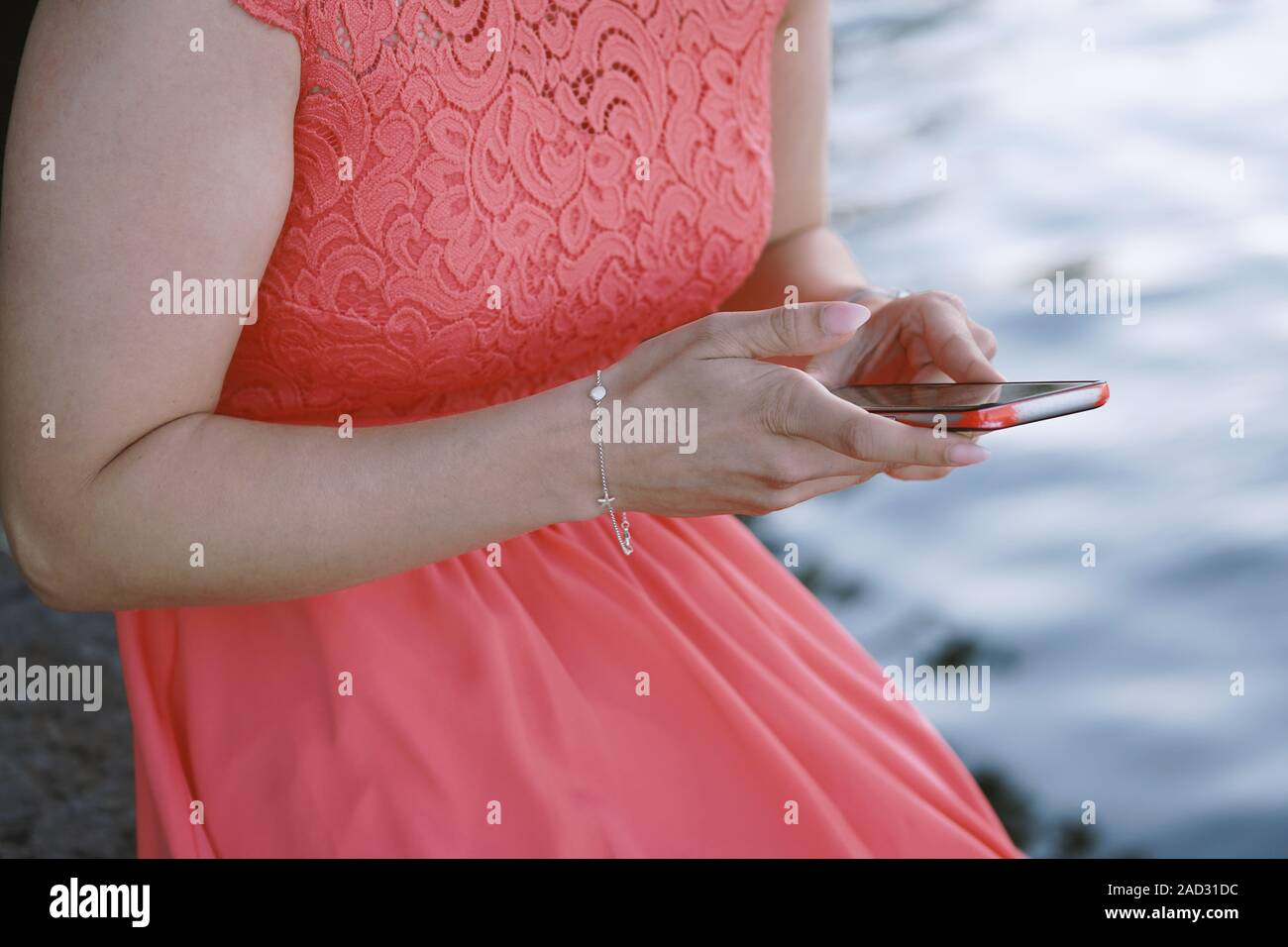Méconnaissable jeune femme assise au bord de l'eau à l'aide de son téléphone intelligent ou mobile Banque D'Images