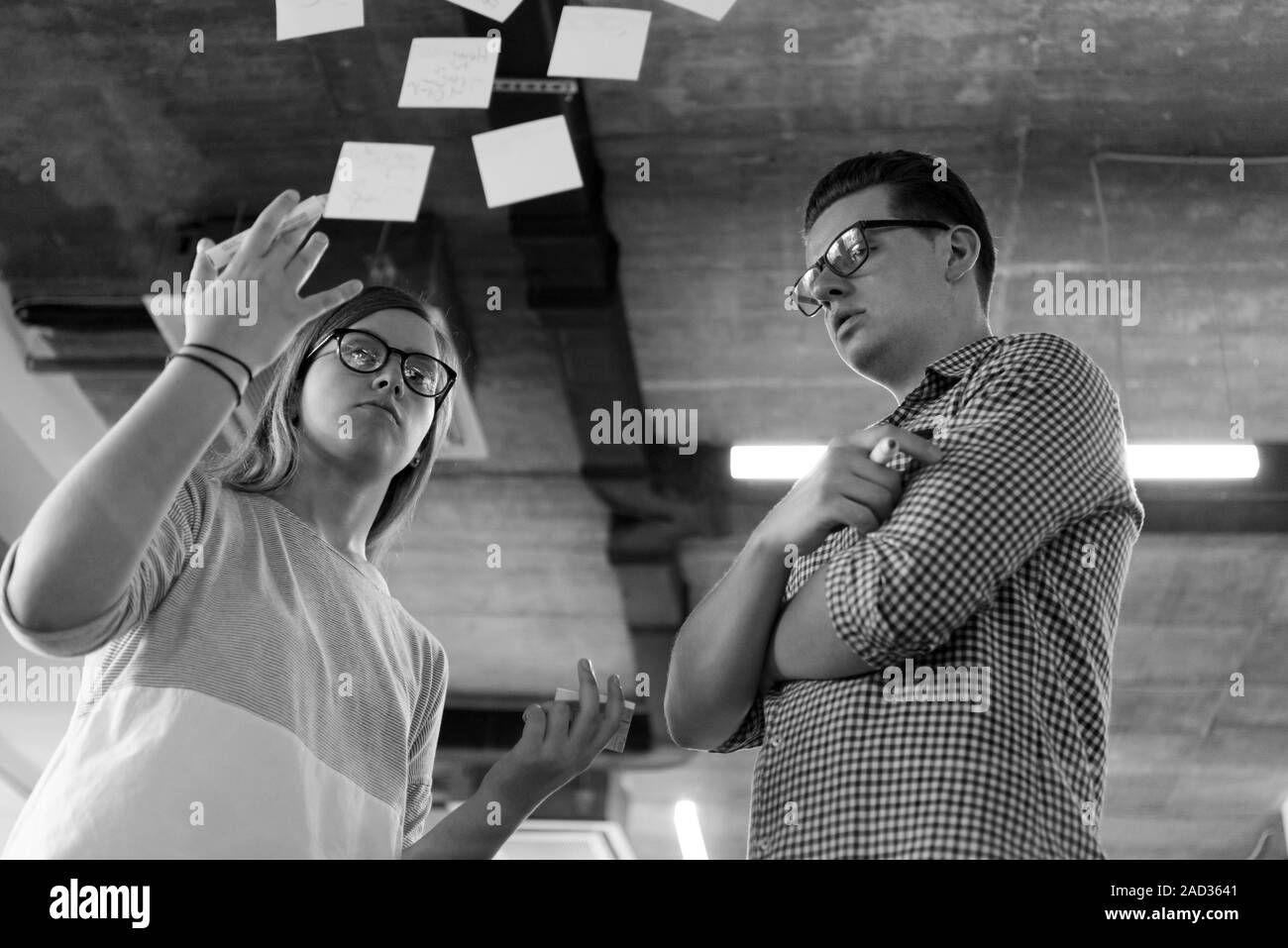 Jeune couple à l'intérieur de bureaux modernes à écrire des notes sur des autocollants Banque D'Images