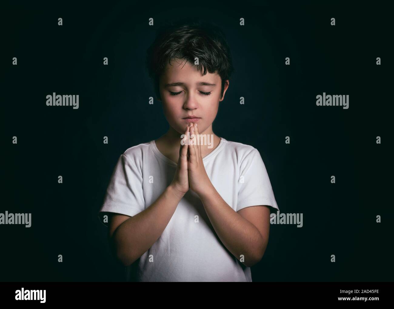 Enfant avec les mains jointes en prière sur fond noir Banque D'Images