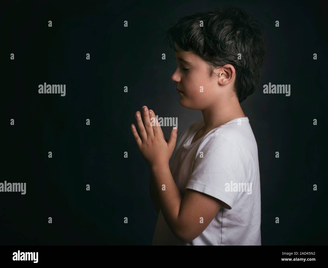 Enfant avec les mains jointes en prière sur fond noir Banque D'Images
