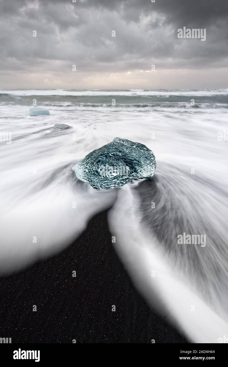 Bloc de glace ronde dans des tons bleus sur une plage avec de fortes vagues, l'eau s'écouler en montre une tendance frappante et traces de mouvement (exposition de longue durée) Banque D'Images