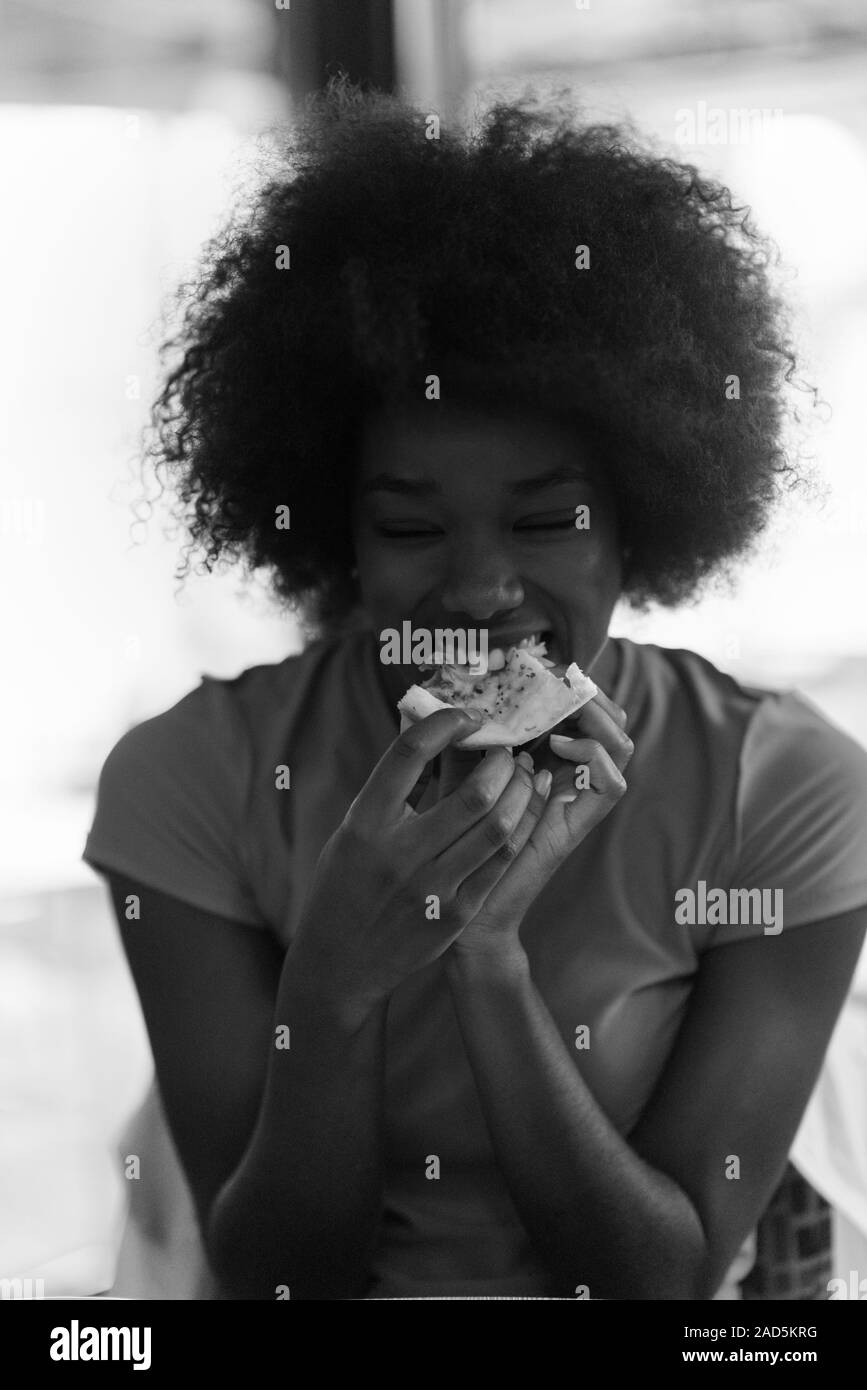 Femme avec la coiffure afro de manger de délicieuses pizza slice Banque D'Images