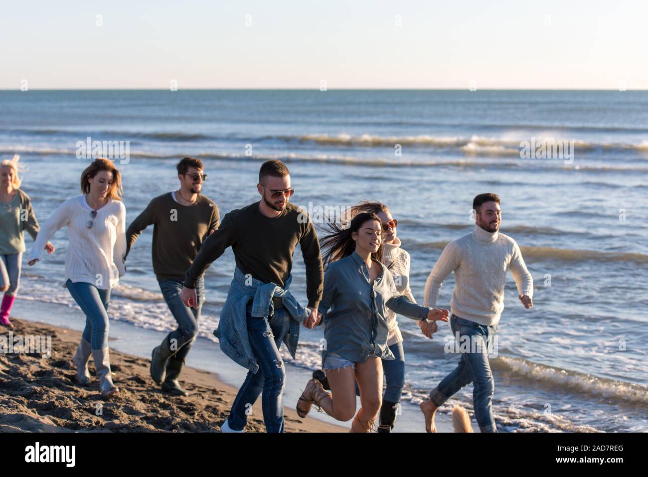 Groupe d'amis s'exécutant sur plage en journée d'automne Banque D'Images