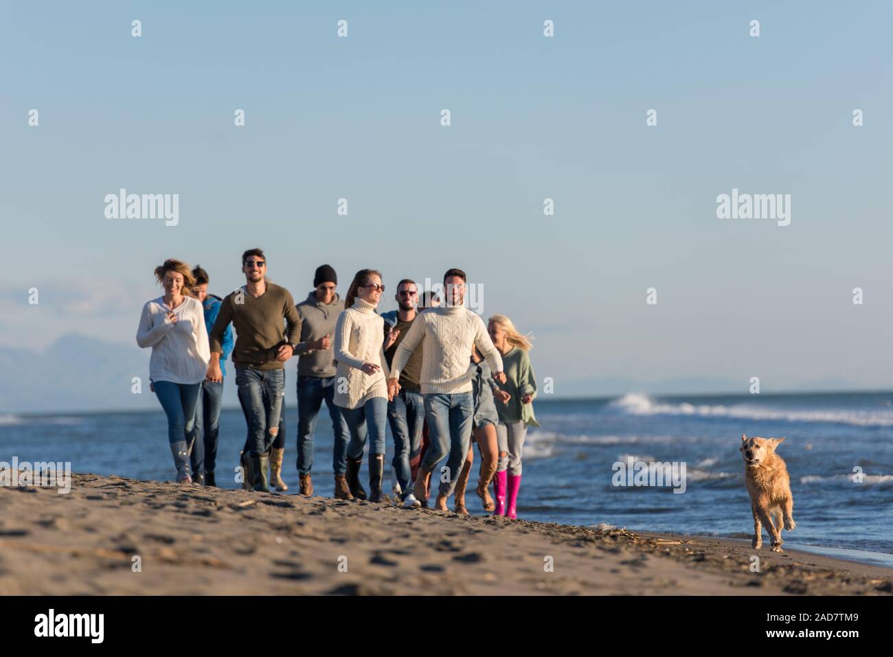 Groupe d'amis s'exécutant sur plage en journée d'automne Banque D'Images