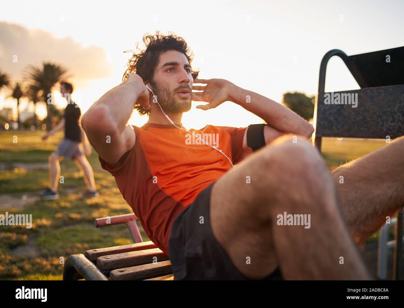 Certain jeune homme écoute de la musique dans les écouteurs de téléphone intelligent armband faisant des exercices sur des équipements publics dans le sport en plein air au parc Banque D'Images
