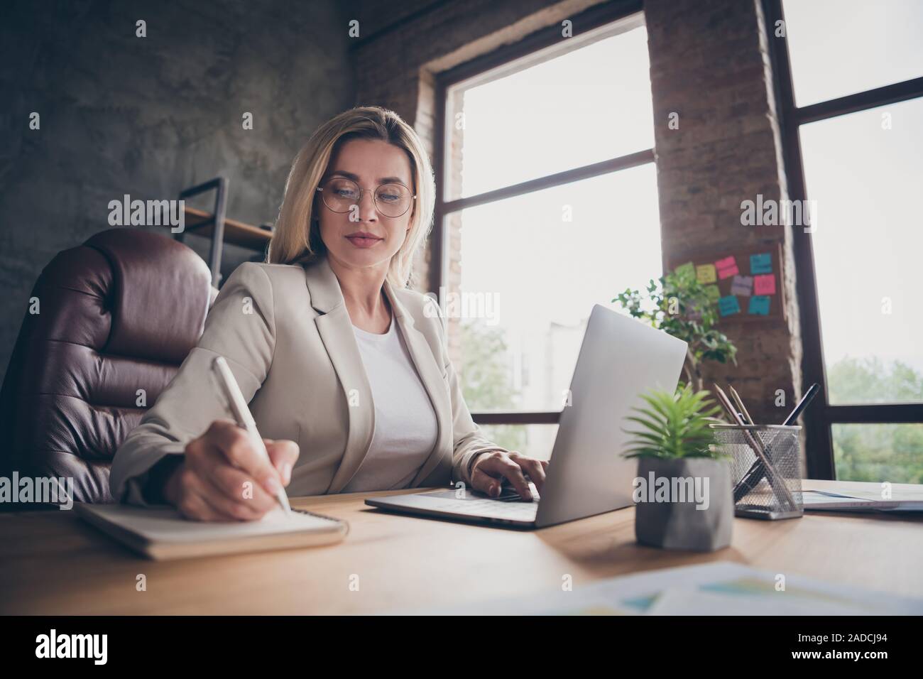 L'angle ci-dessous bas voir photo de femme concentré grave notant la comparaison des données sur l'ordinateur portable avec des données dans l'ordinateur portable Banque D'Images