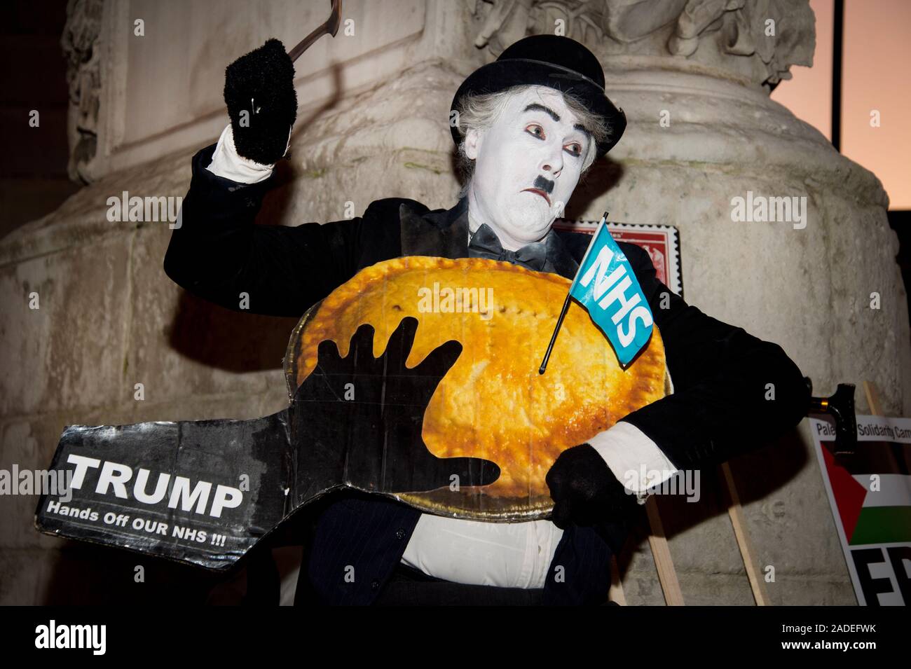 3 décembre 2019 Trafalgar Square. Manifestation anti Trump. Un homme habillé comme Charlie Chaplin est titulaire d'une photo d'un diagramme circulaire appelée NHS et une main d'essayer Banque D'Images