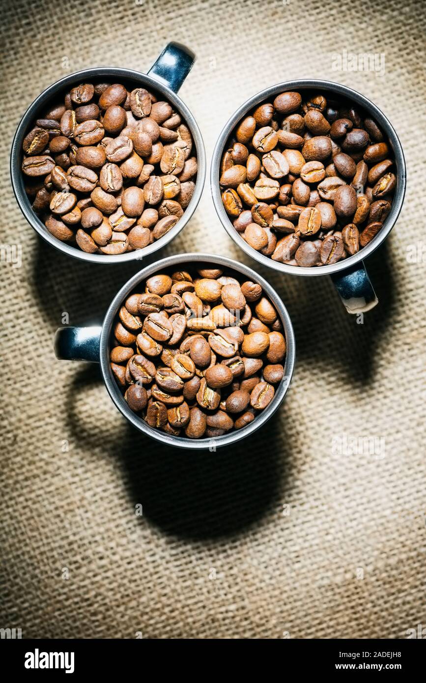 Les frais généraux de droit de trois tasses en métal pleine de grains de café torréfiés sur un fond de toile de jute. Banque D'Images