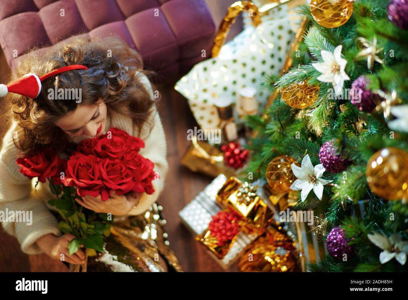 Vue supérieure de smiling 40 ans femme au foyer avec de longs cheveux de brunette en or paillette jupe et pull blanc sous l'arbre de Noël décoré près de l'actuelle Banque D'Images