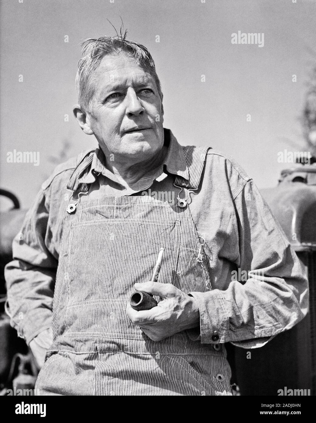 1940 Portrait d'agriculteurs d'âge moyen à l'extérieur en s'APPUYANT SUR LE TRACTEUR AVEC UNE PIPE PORTANT HICKORY STRIPE SALOPETTE - f7989 HAR001 HARS BRETELLES HOMMES AGRICULTURE EXPRESSIONS DE CONFIANCE L'AGRICULTURE D'ÂGE MOYEN B&W HOMME D'ÂGE MOYEN OLDSTERS OBJECTIFS FORCE ANTIQUE TOBACCO AGRICULTEURS EXPÉRIMENTÉS LOW ANGLE FIERTÉ ANCIENS BIB EN NOYER NOIR ET BLANC DE LA CROISSANCE DE L'ORIGINE ETHNIQUE CAUCASIENNE HAR001 old fashioned Banque D'Images