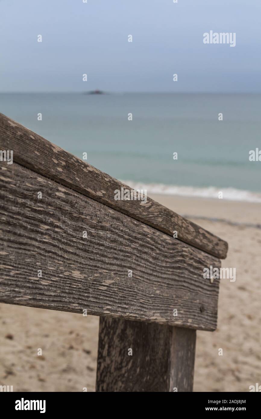 Détail de la balustrades en bois patiné à l'entrée de la plage de la ville. Ligne de sable, mer méditerranée avec de petites vagues et un horizon. Ciel nuageux. Banque D'Images