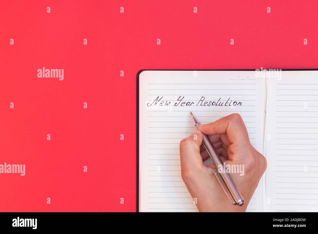 Vue directement au-dessus de la main de femme écrit mots nouvelle année Résolution dans un bloc-notes sur fond rouge Banque D'Images