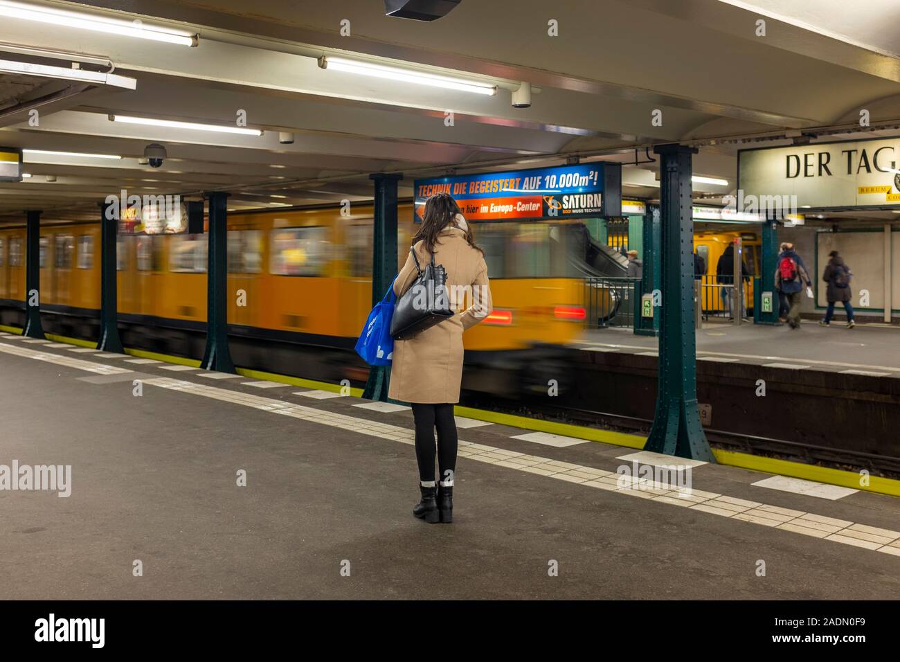 Jeune femme en manteau de chameau attend sur la plate-forme de la station de métro de Berlin- motion blur Banque D'Images