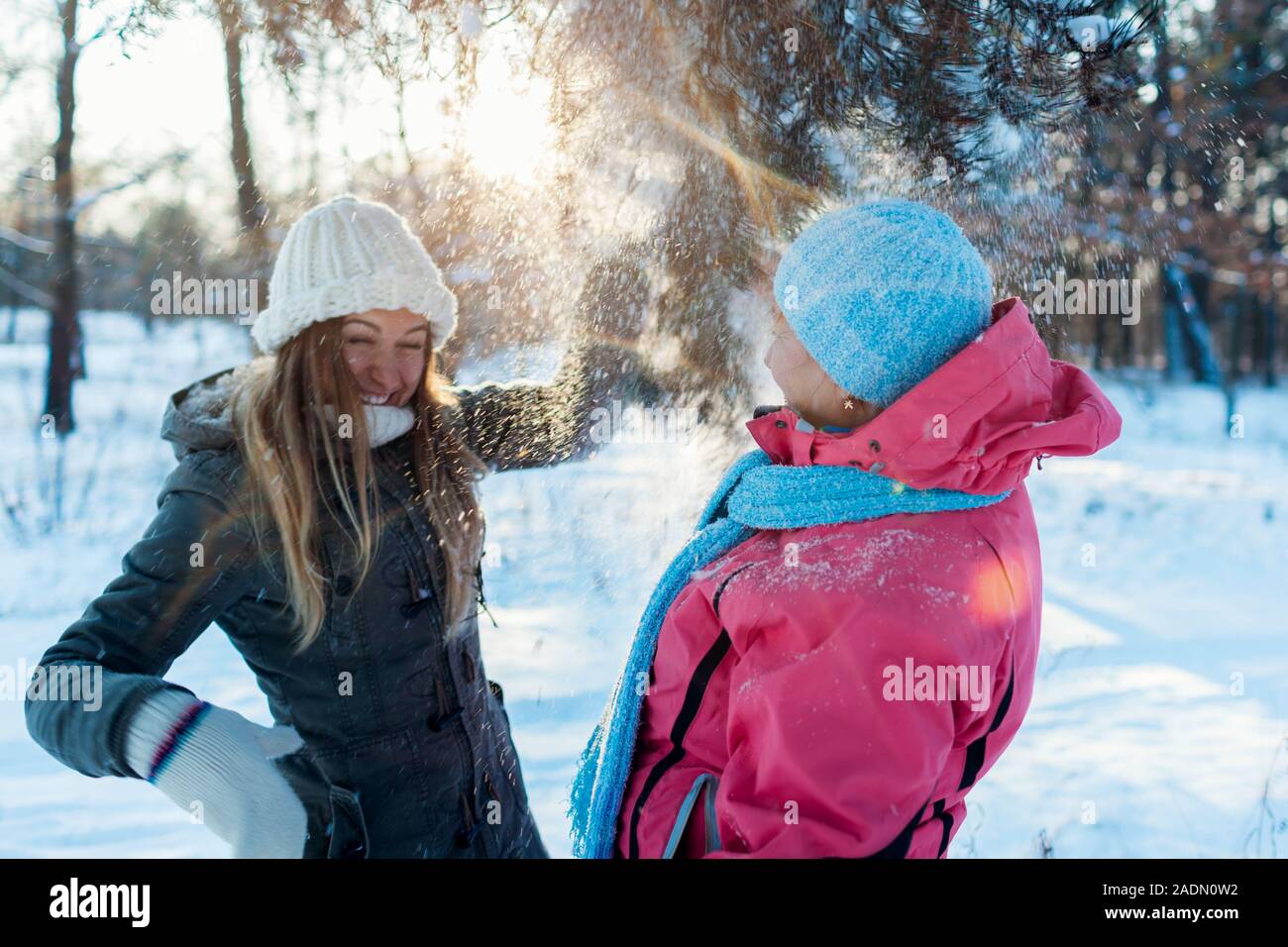 Activités d'hiver. Mère et fille adultes secouant branches avec de la neige à l'extérieur. Pour des vacances de détente en famille Banque D'Images