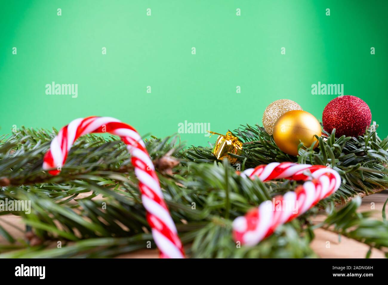 Branches de sapin vert avec des ornements de Noël (boules de Noël, des cannes de bonbon, présente, fir cone) sur une table en bois devant un fond vert avec Banque D'Images