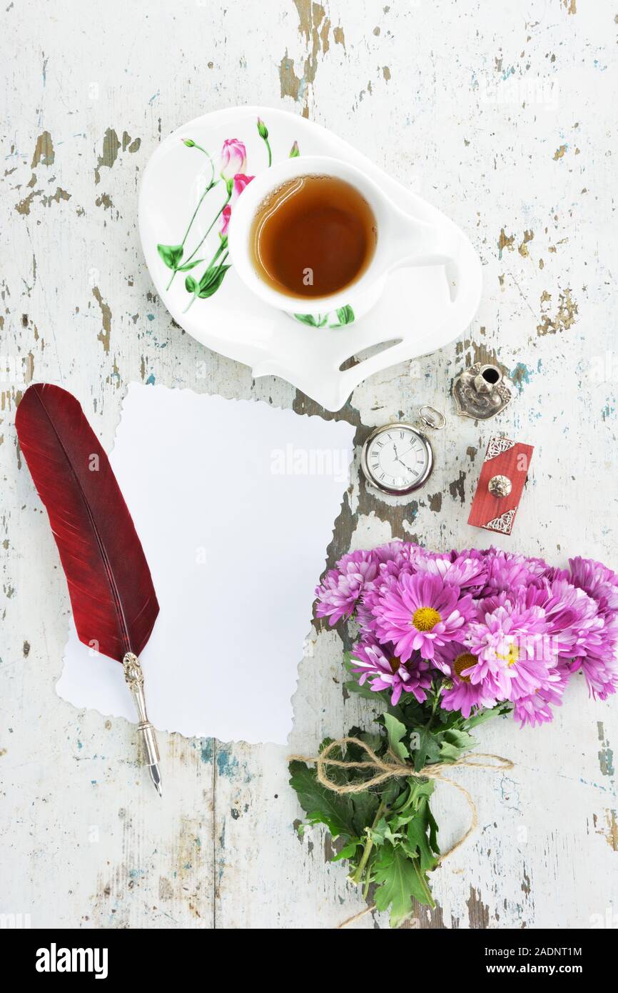 Plume avec plume rouge profond, Quill stand,un buvard,un papier blanc ,une vieille montre de poche, un bouquet de chrysanthèmes violets et tasse de thé avec matchin Banque D'Images