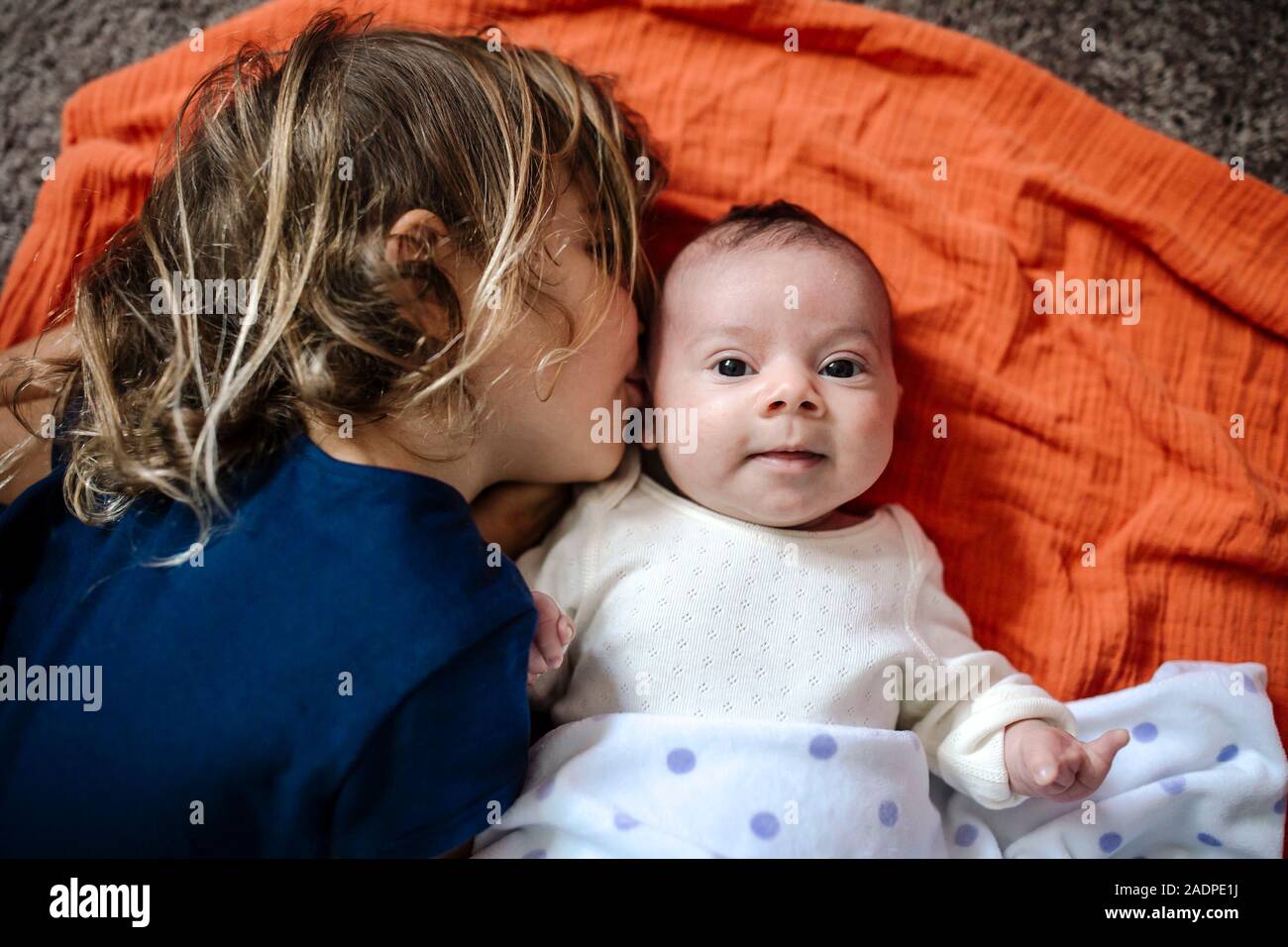 4 yr old kissing happy baby sister sur couverture orange sur marbre Banque D'Images
