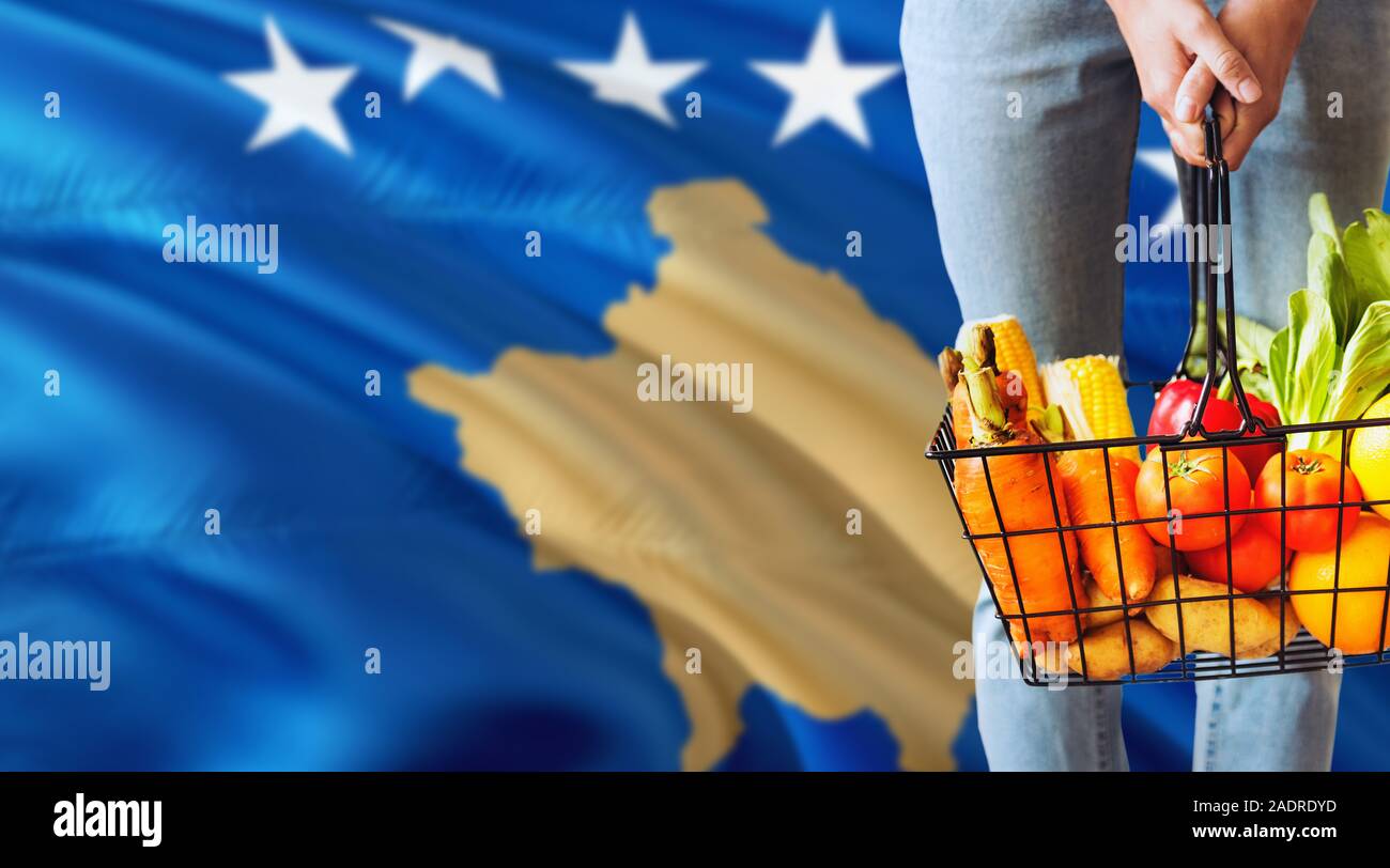 Woman is holding supermarché panier, Kosovo waving flag background. Concept de l'économie pour les fruits et légumes. Banque D'Images