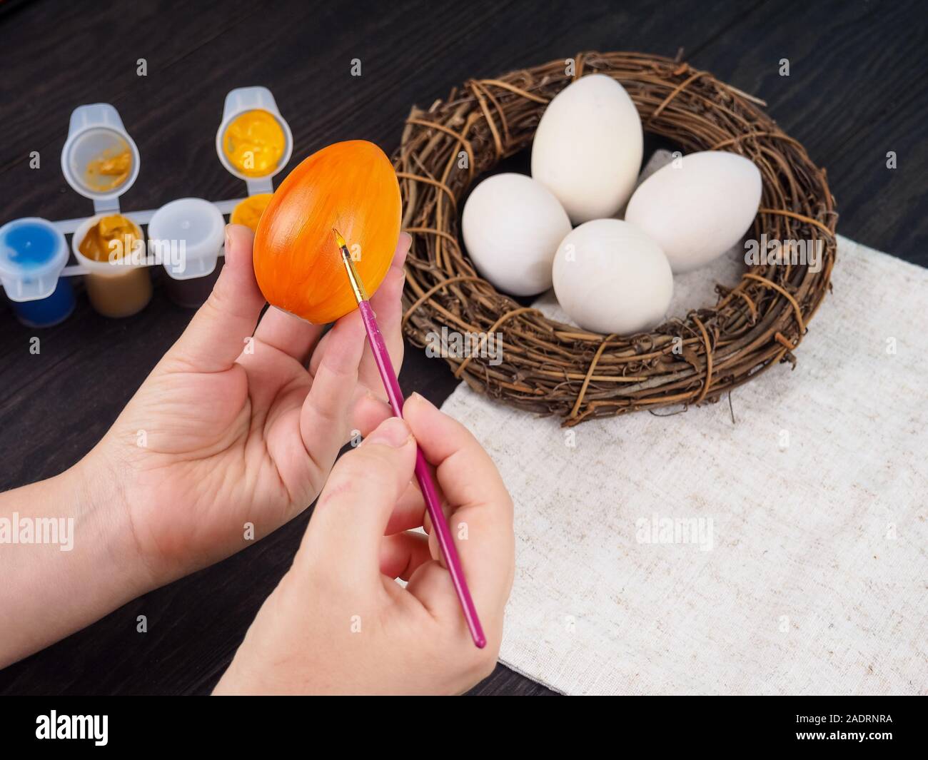 Gros plan des mains de femme peignant un oeuf de pâques sur fond de bois. Les mains de femme peignant l'oeuf de pâques en bois avec la brosse. Le concept de fait à la main et Banque D'Images