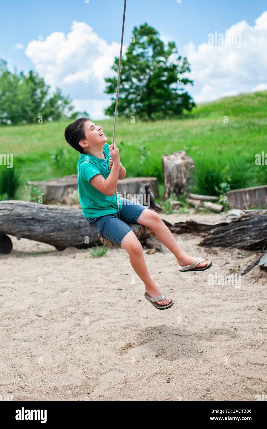 Garçon 7-8 ans swinging sur tree swing rire extérieur en été Banque D'Images