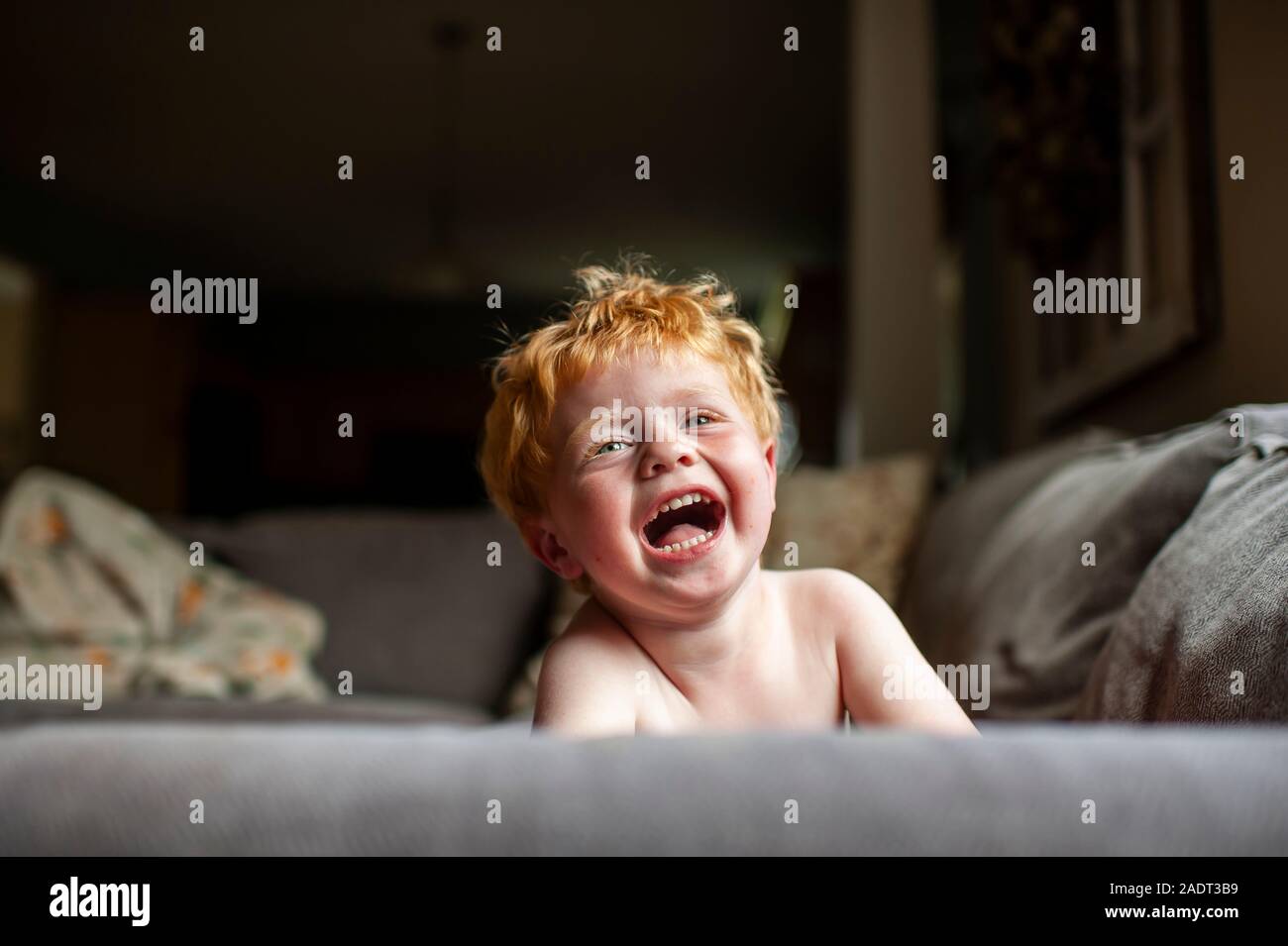 Bébé garçon aux cheveux rouges en riant tout en posant sur la table à la maison Banque D'Images