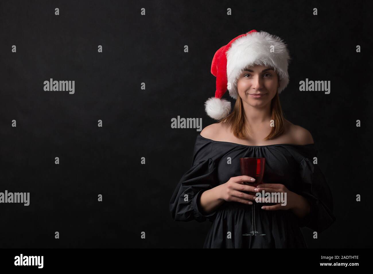 Une fille dans un santa hat soulève un verre de rouge avec un toast pour la maison de vacances sur un fond noir. Concept pour cartes postales, dépliants, invitations, annonces ab Banque D'Images
