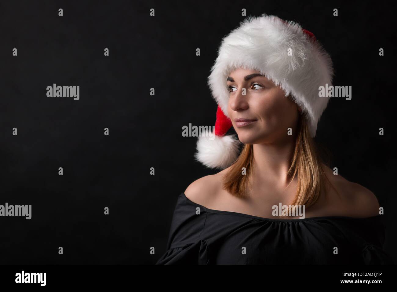 Fille charmante à santa hat à gauche, gros plan sur un fond sombre. Notion de bonne année carte de voeux, avec place pour le texte. Banque D'Images