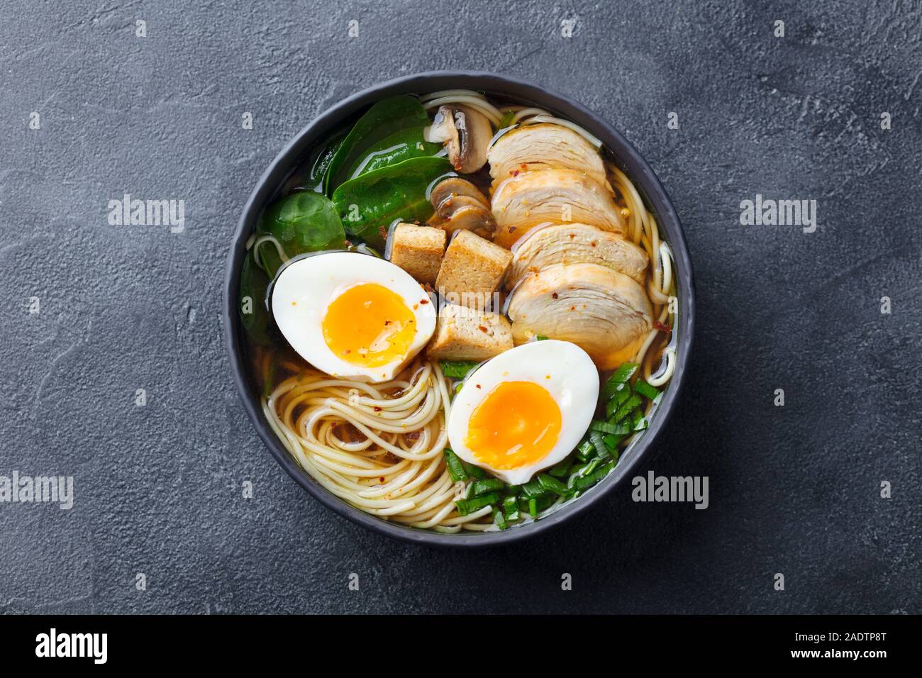 Soupe de nouilles asiatiques, ramen avec du poulet, tofu, légumes et d'oeuf dans un bol noir. Vue d'en haut. Copier l'espace. Fond d'Ardoise Banque D'Images