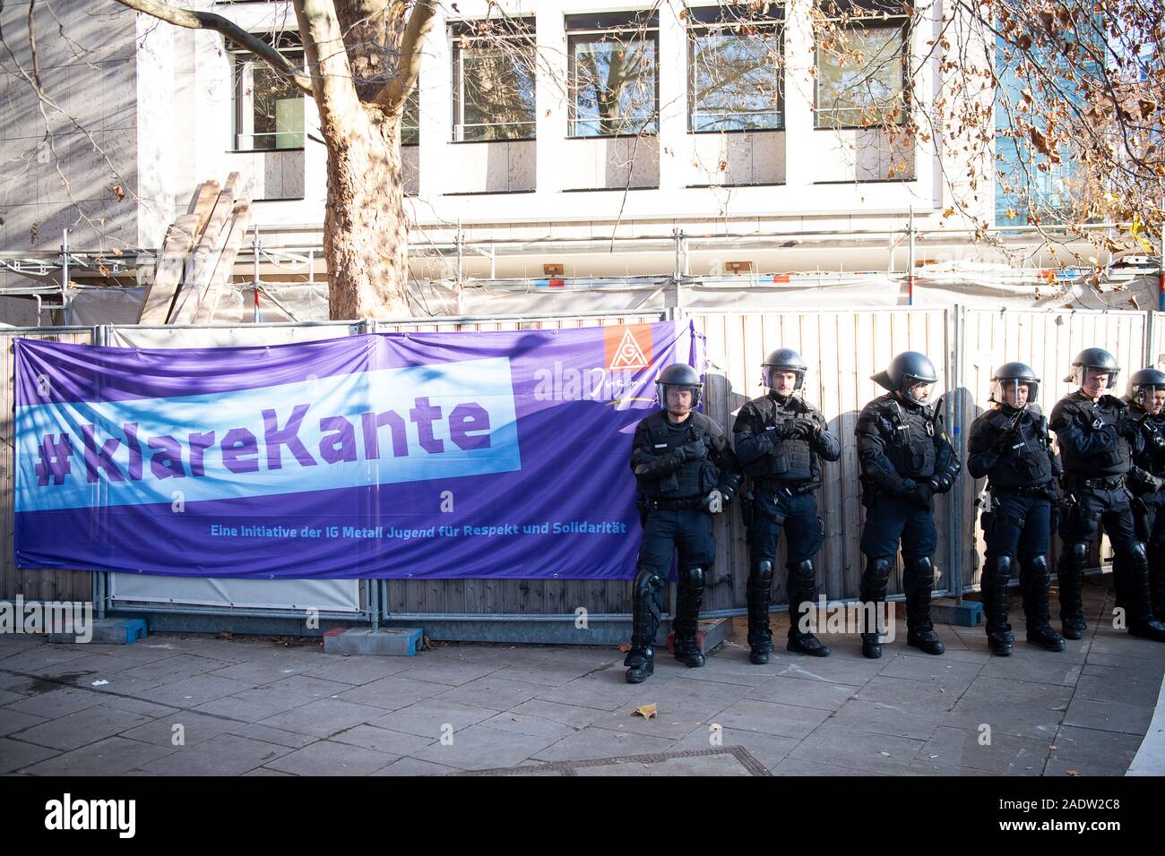 Stuttgart, Allemagne. Le 05 mai 2019. Au début du procès sur le cas d'un employé qui a été congédié de Daimler pour avoir insulté un collègue turc, des agents de police se tenir devant le tribunal du travail de l'état de Bade-Wurtemberg à côté d'une bannière de l'IG Metall. Le Tribunal du travail, comme la première instance, a considéré le licenciement d'être licite. (Az. 11 Ca 3738/18, décision du 29.11.2018) Crédit : Sebastian Gollnow/dpa/Alamy Live News Banque D'Images