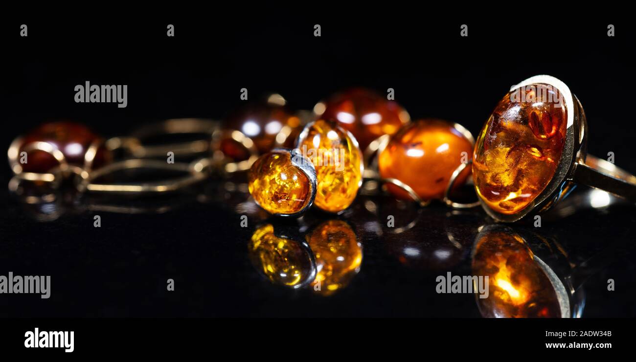Panorama de bijoux avec des pierres d'ambre Collier en ambre, bague et boucle d'oreille et pendentif avec noble métal comme l'or, en face d'un fond noir sur un bla Banque D'Images