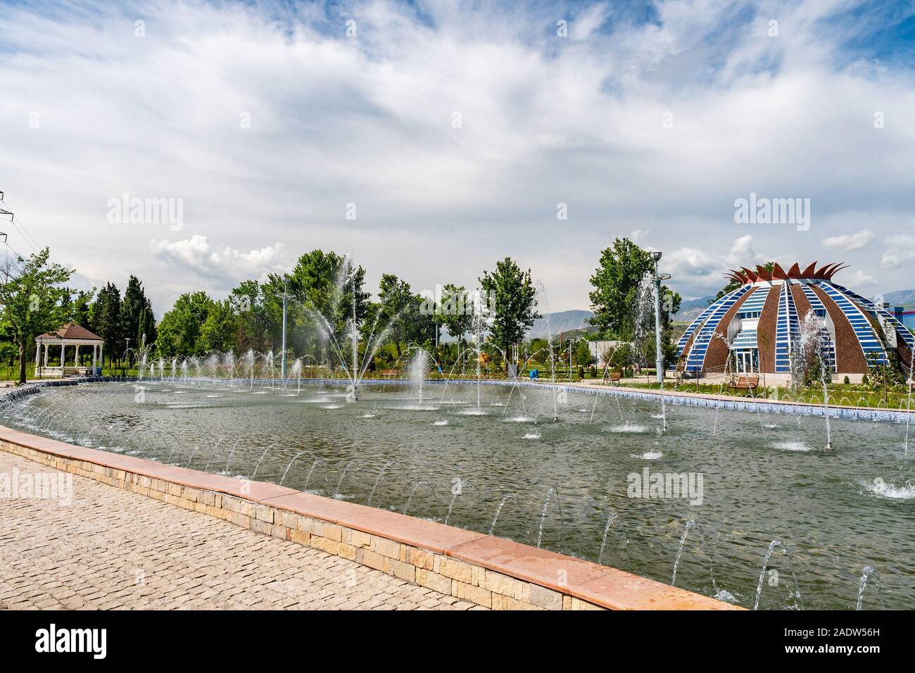 Douchanbé Youth Park vue pittoresque de maison en forme de grenade et bassin avec jets d'eau sur un ciel bleu ensoleillé Jour Banque D'Images