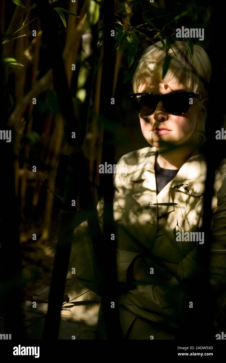 Jeune femme élégante, 20's style des années 1950, le port de lunettes de soleil, imperméable et vu par le feuillage Banque D'Images