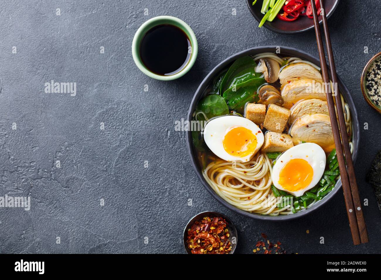Soupe de nouilles asiatiques, ramen avec du poulet, tofu, légumes et d'oeuf dans un bol noir. Fond d'ardoise. Close up. Vue d'en haut. Banque D'Images