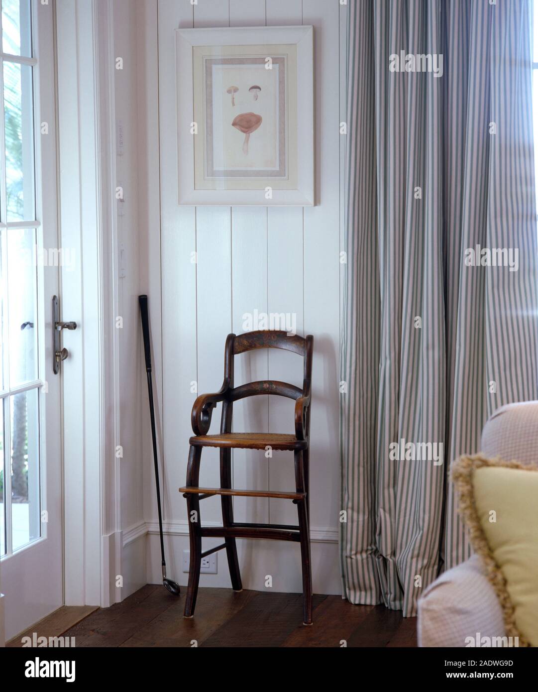 Chaise haute enfant's antique contre un mur lambrissé blanc blanc dans un salon avec des rideaux à rayures Banque D'Images