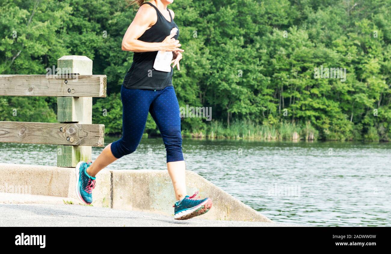 Une des femmes est l'exécution d'une course de 10K dans un parc, en traversant un pont à côté d'southards étang avec des arbres en arrière-plan. Banque D'Images