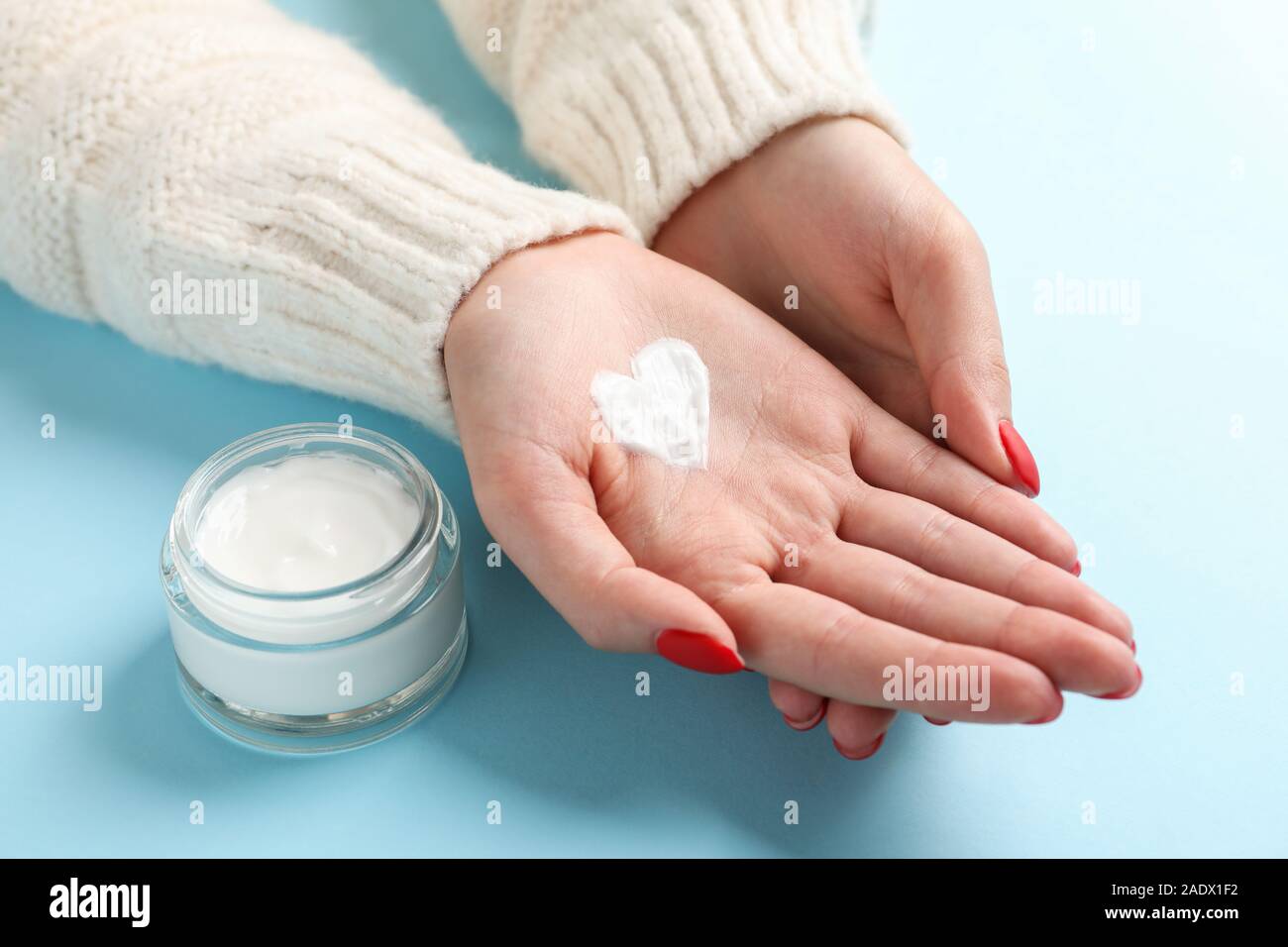 Femme mains, forme de cœur créé à partir de l'hiver, pot de crème pour la peau crème d'hiver sur fond bleu. Un espace réservé au texte Banque D'Images