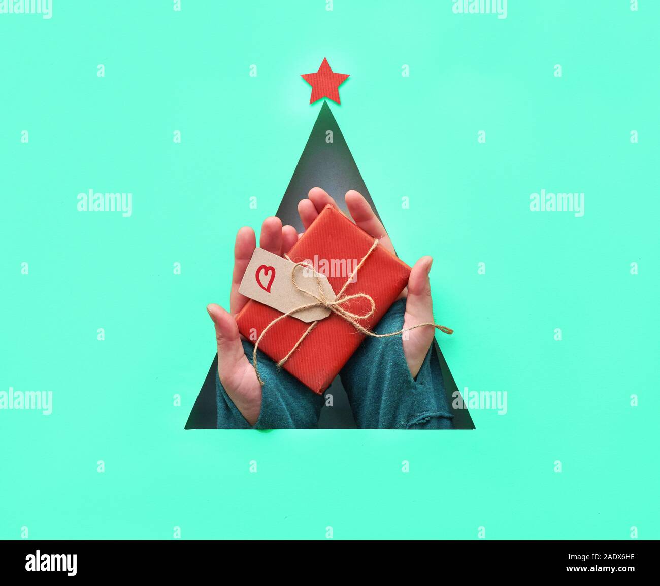 Creative géométrique télévision Noël réside dans l'aqua mode menthe et nuances de couleur rouge flamme, cyan et rouge. Hands holding wrapped gift in triangul Banque D'Images