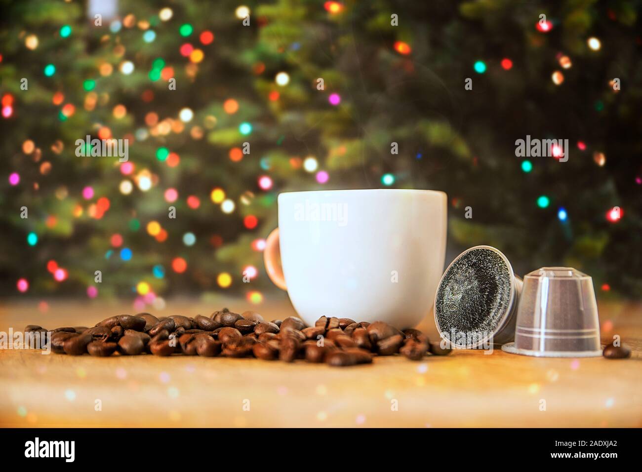 Les capsules de café à côté d'une tasse de café chaud et de fumée sur une table de bois contre une lumière de Noël Décoration. Copie vide de l'espace pour l'éditeur de texte. Banque D'Images