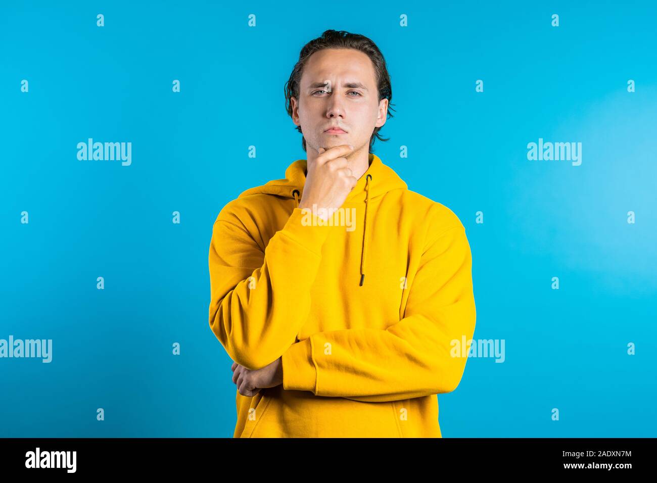 Penser l'homme à la recherche sur fond bleu. Inquiets face contemplative des expressions. Beau modèle masculin en jaune Banque D'Images