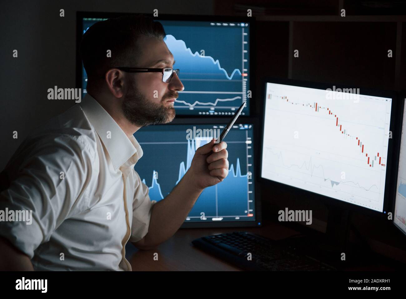 Conception d'échange. Homme barbu en chemise blanche travaille au bureau avec plusieurs écrans d'ordinateur dans les tableaux d'index Banque D'Images