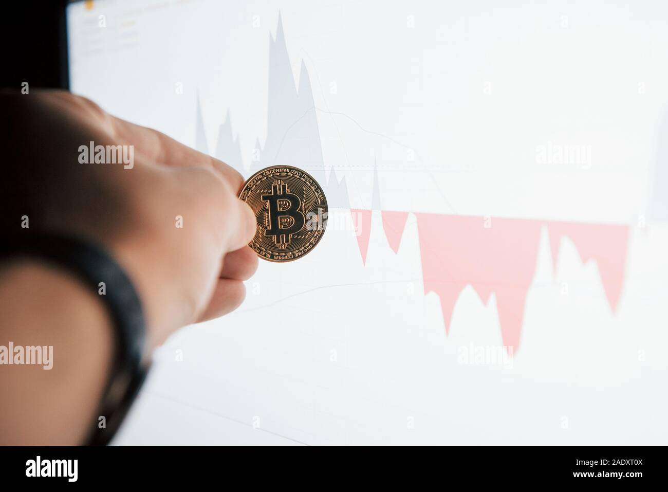 Man's hand holding en bitcoin contre bureau moderne avec moniteur graphique Banque D'Images