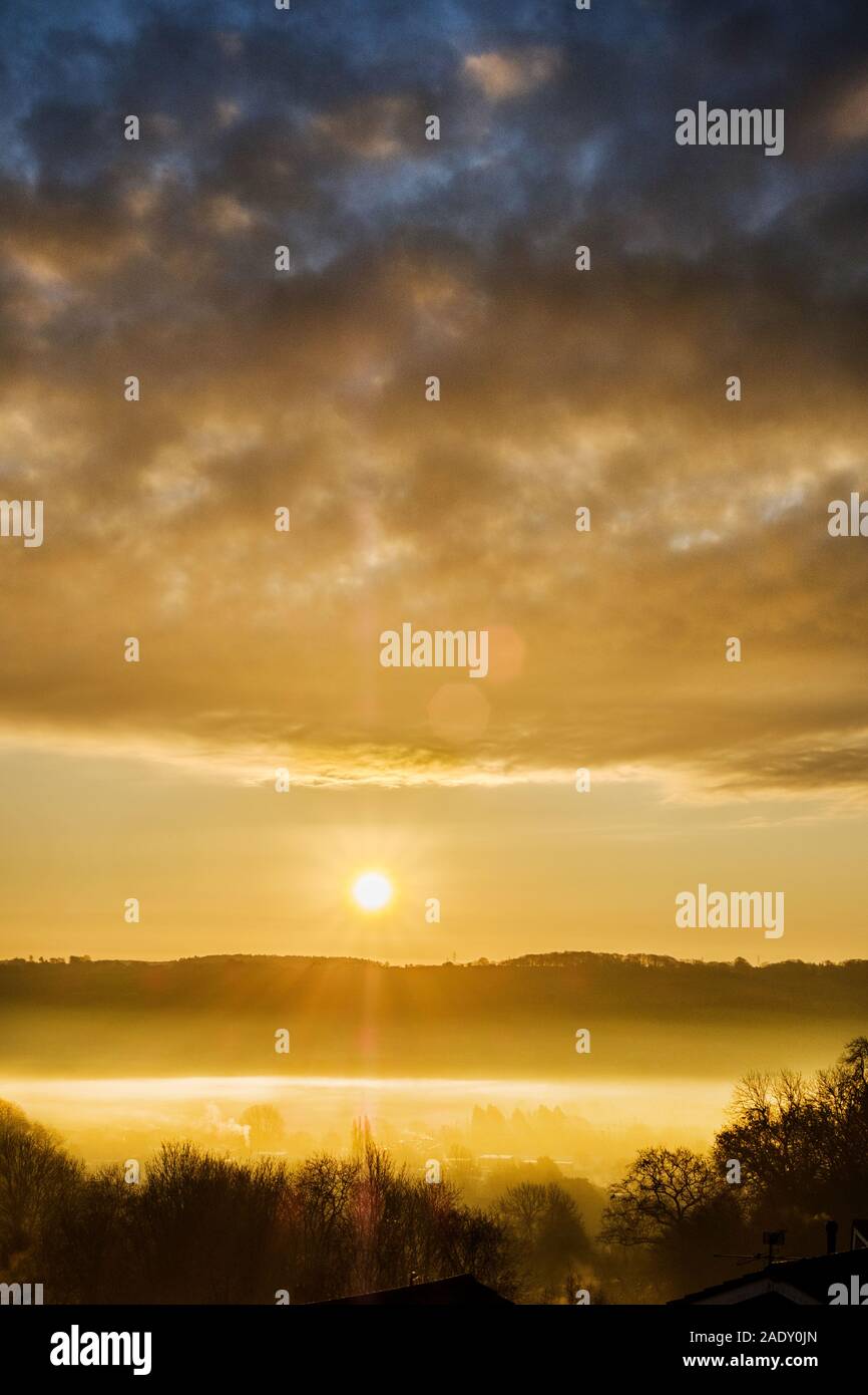 Un magnifique lever du soleil d'hiver spectaculaire, à travers une vallée remplie de brouillard. Le soleil levant est capturé entre un lointain Hill et de nuages bas au-dessus de la vallée du brouillard Banque D'Images