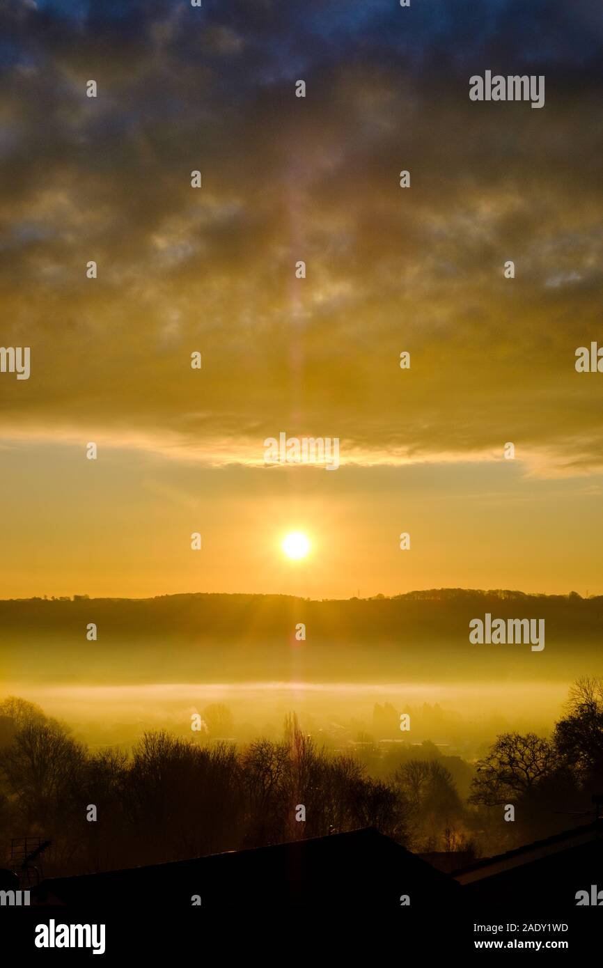 Un magnifique lever du soleil d'hiver spectaculaire, à travers une vallée remplie de brouillard. Le soleil levant est capturé entre un lointain Hill et de nuages bas au-dessus de la vallée du brouillard Banque D'Images