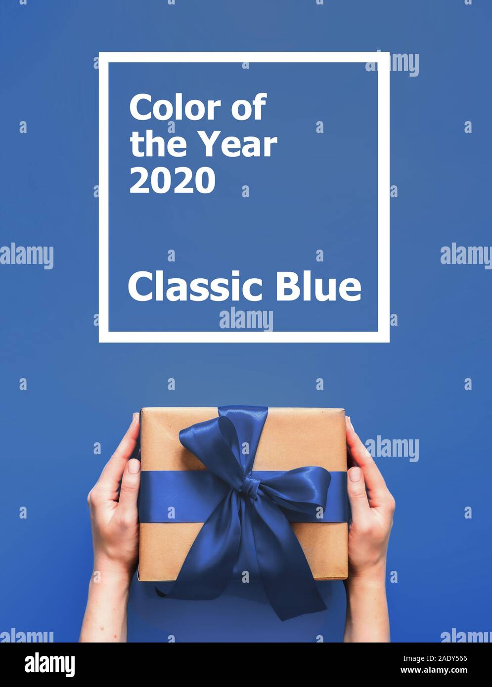 Boîte cadeau femme mains tiennent sur fond bleu avec les mots de l'année 2020 Couleur bleu classique. Boîte-cadeau dans l'artisanat du papier d'emballage avec ruban de satin bleu. La verticale. Banque D'Images