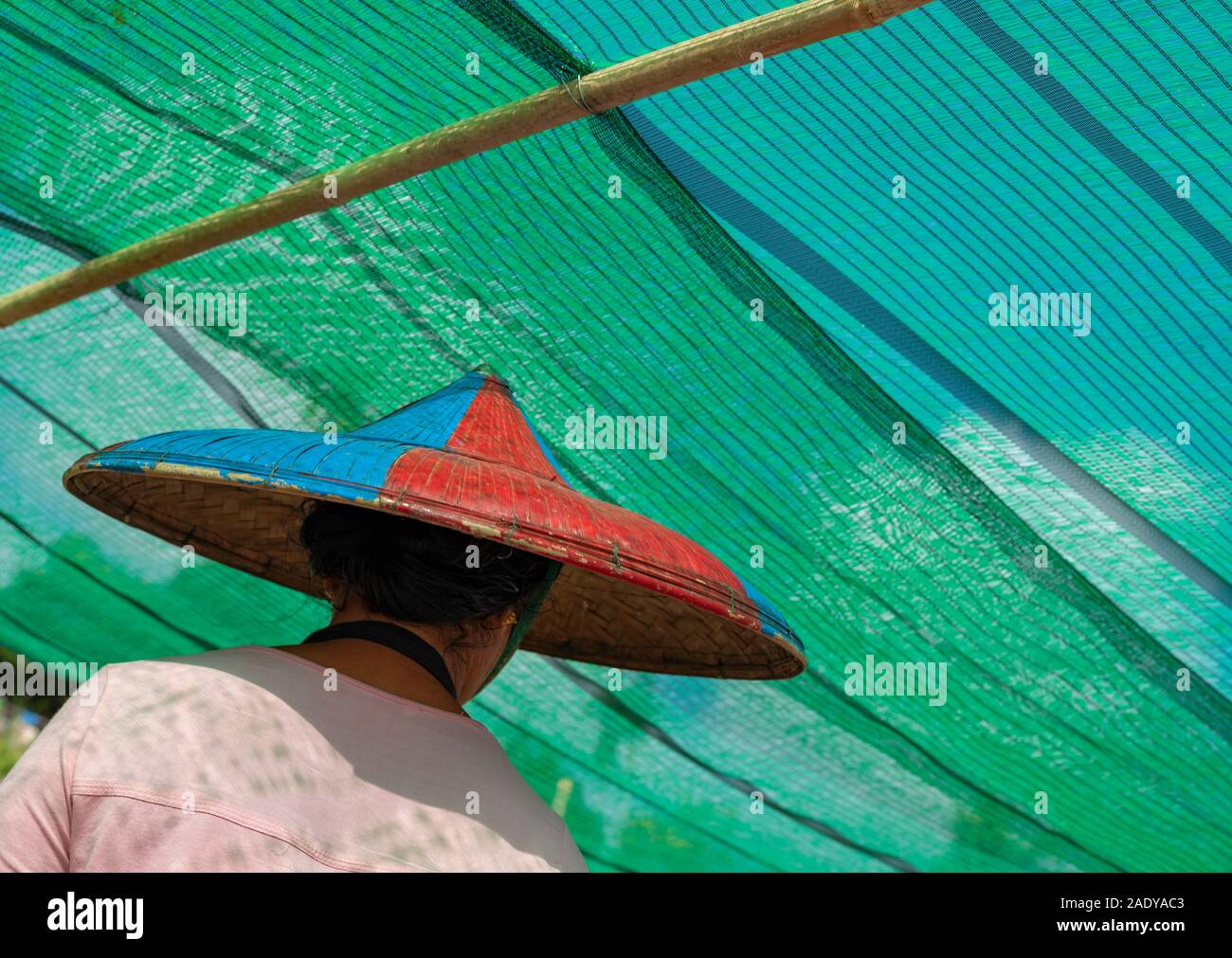 Femme birmane dans un chapeau de riz conique peint en rouge et bleu quitte un ferry en vertu de la couleur turquoise de l'écran solaire sur le pont principal sur la rivière Chindwin Banque D'Images