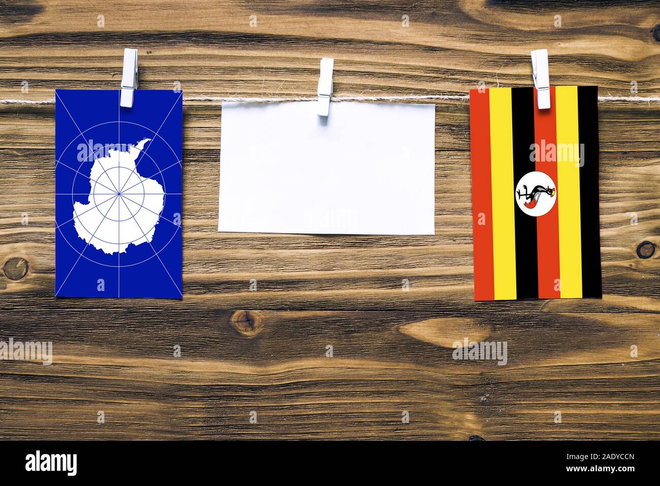 Drapeaux suspendus de l'Antarctique et de l'Ouganda attaché à corde avec pinces à linge avec de l'espace de copie sur papier blanc sur fond de bois.rapport diplomatique Banque D'Images