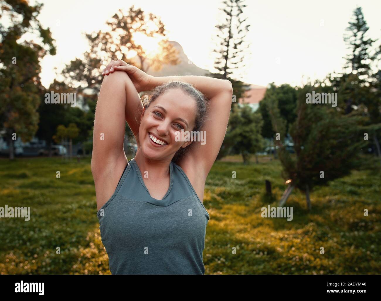 Portrait of a smiling sporty woman stretching her arms dans le parc Banque D'Images