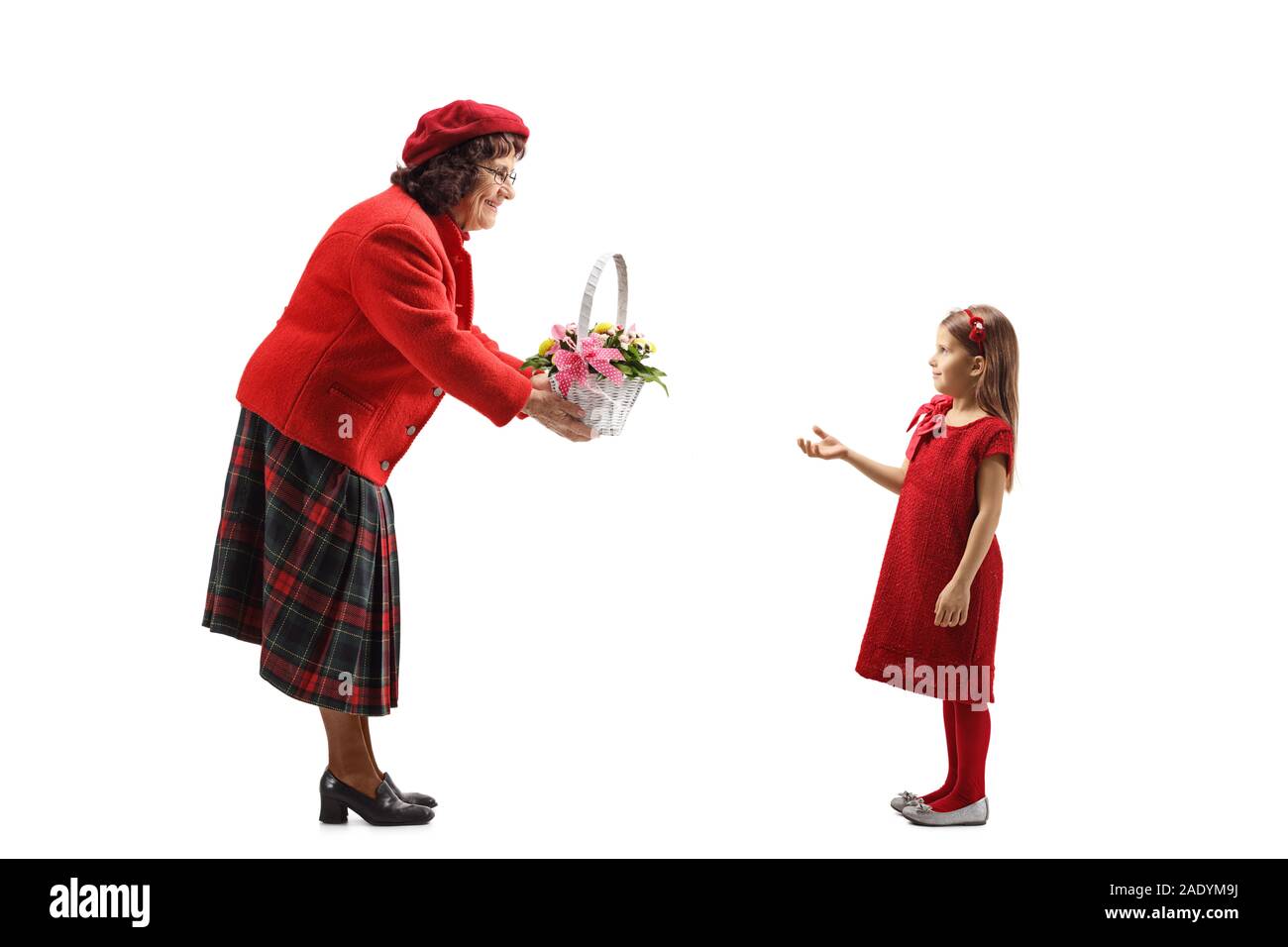 Profil de pleine longueur tourné d'une femme âgée en donnant un panier de fleurs à une petite fille isolée sur fond blanc Banque D'Images