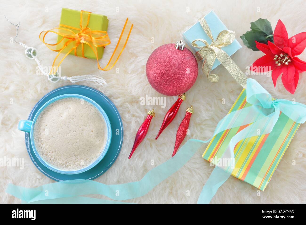 Ornements de Noël ,café avec de la mousse et de petits cadeaux avec des rubans et un poinsettia artificiel fleur sur tapis en peau de mouton Banque D'Images