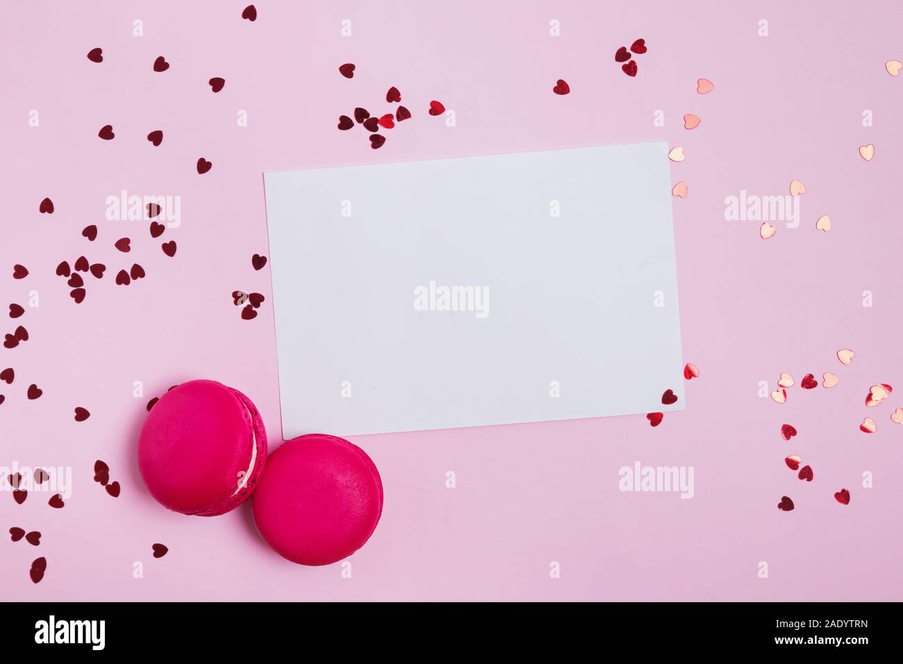 Papier blanc, macarons et confettis en forme de coeur sur fond rose Banque D'Images
